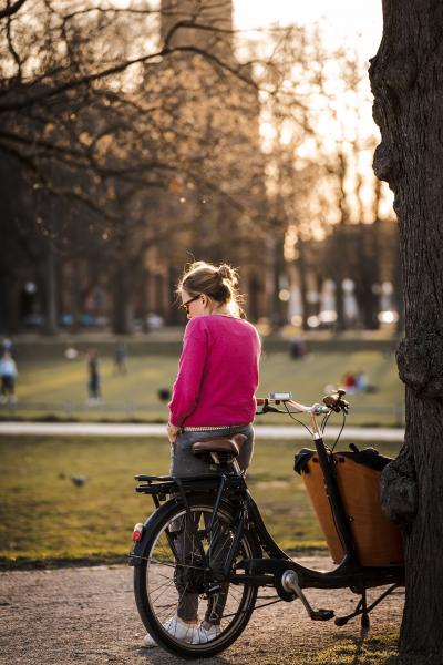 Cargo bike in the park Woman in pink sweater standing next to a cargo bike in a park